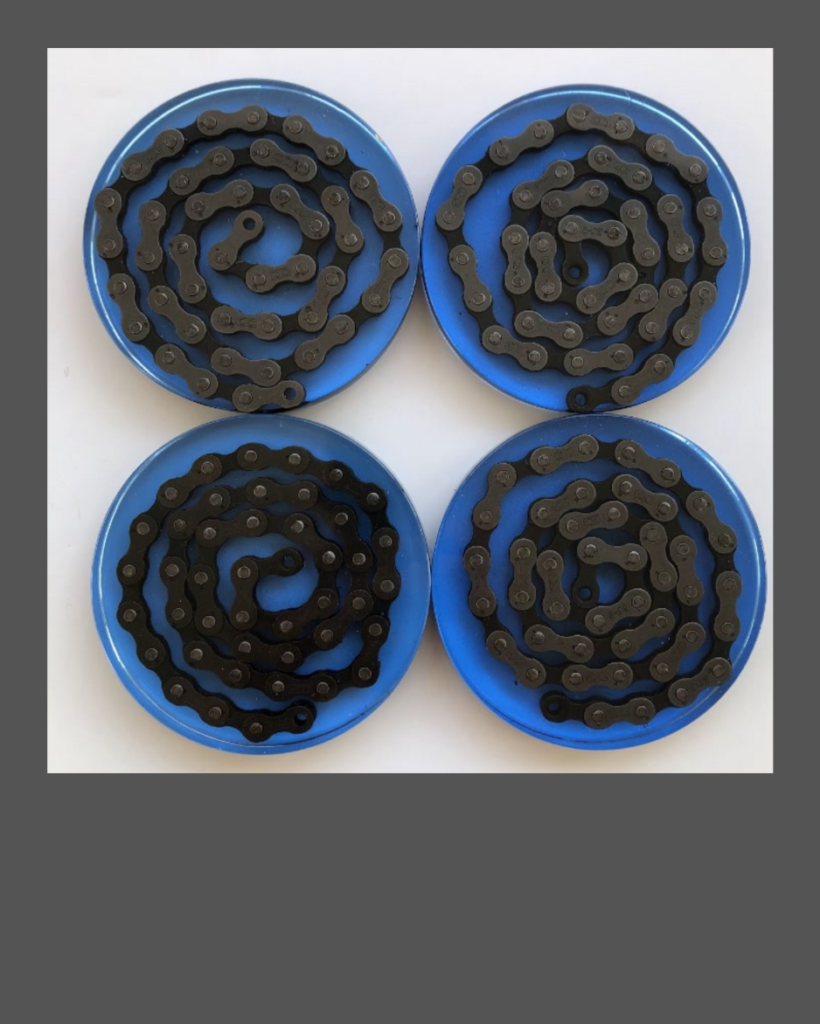 Four beverage coasters made of bright blue epoxy resin containing a spiral of bicycle chain.
