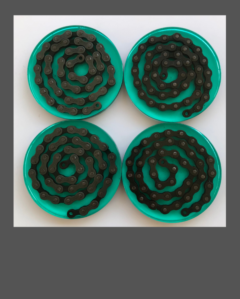 Four beverage coasters made of bright green epoxy resin containing a spiral of bicycle chain.