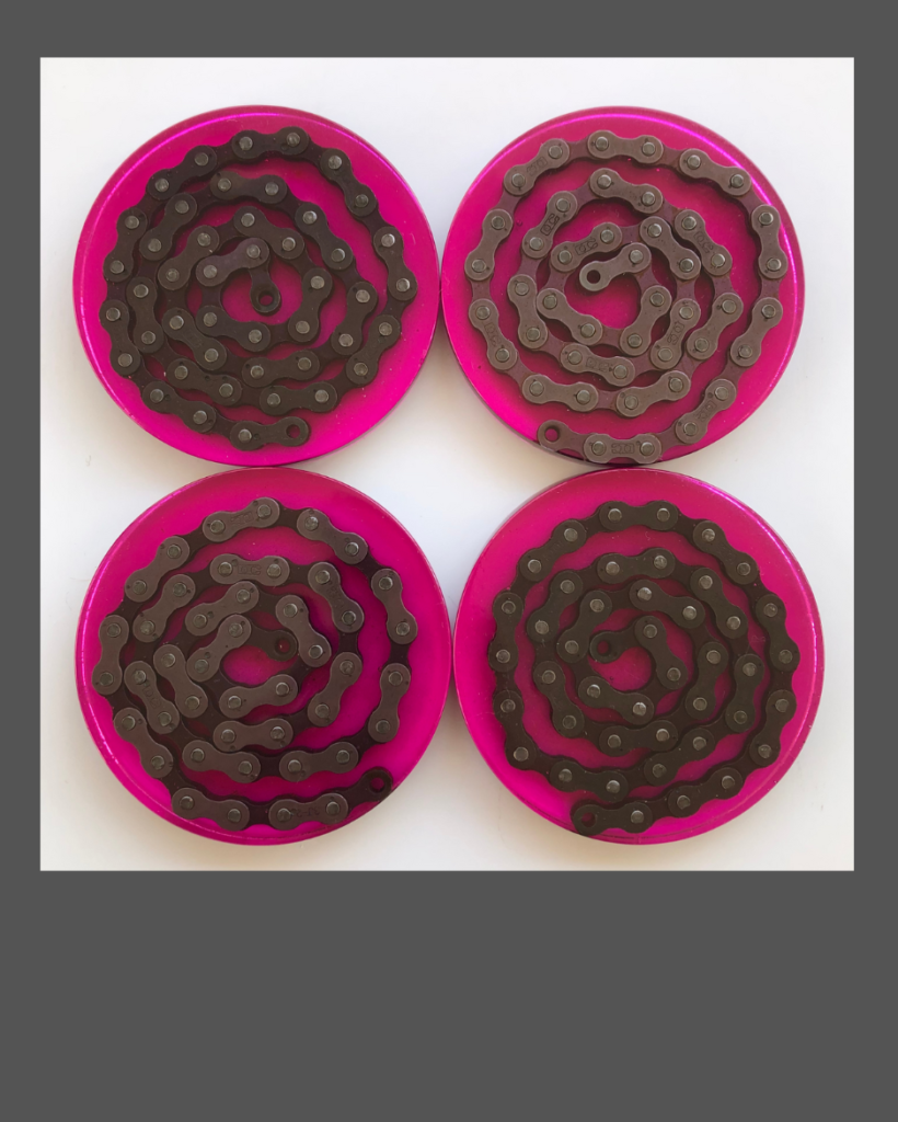 Four beverage coasters made of bright pink epoxy resin containing a spiral of bicycle chain.