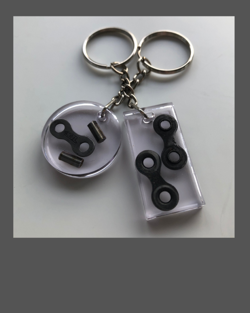 Two keychains made of light purple epoxy resin containing pieces of bicycle chain.